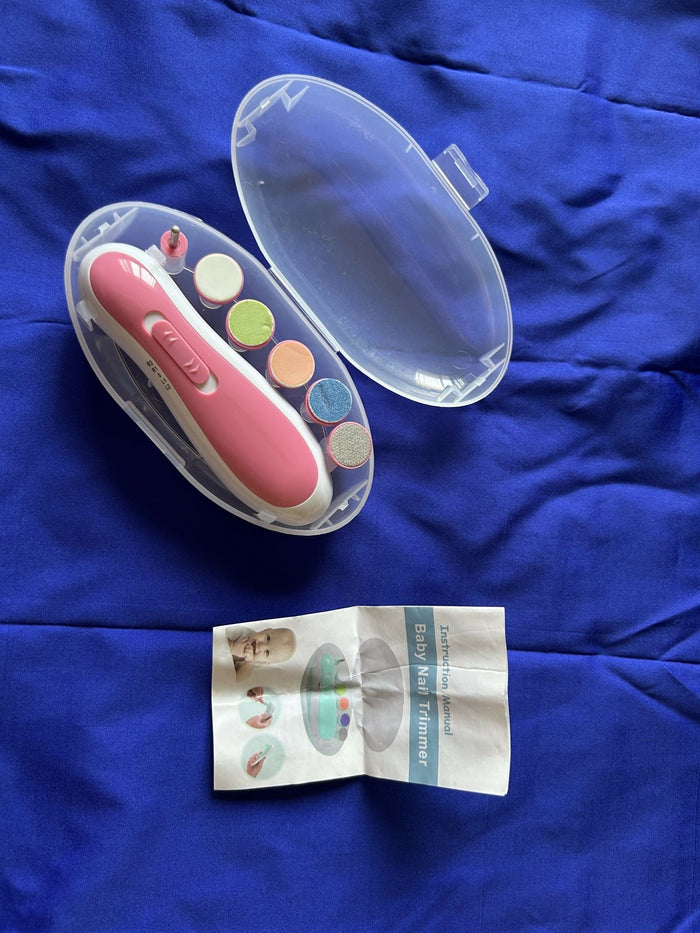 Pink nail clipper with colorful nail pads and instruction sheet on a blue fabric background
