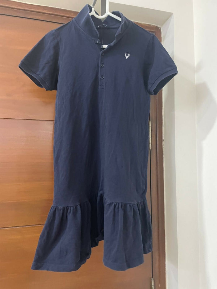 Navy blue dress with a brand logo on a hanger against a wooden door.