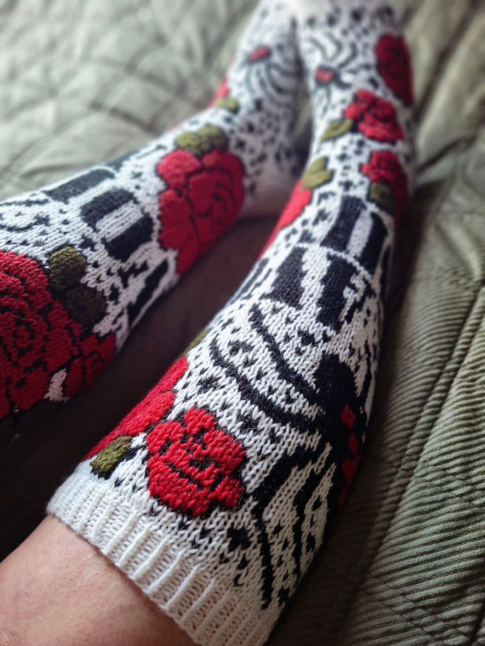 A close-up of a person's legs wearing white knit socks with a black geometric pattern and red rose motifs