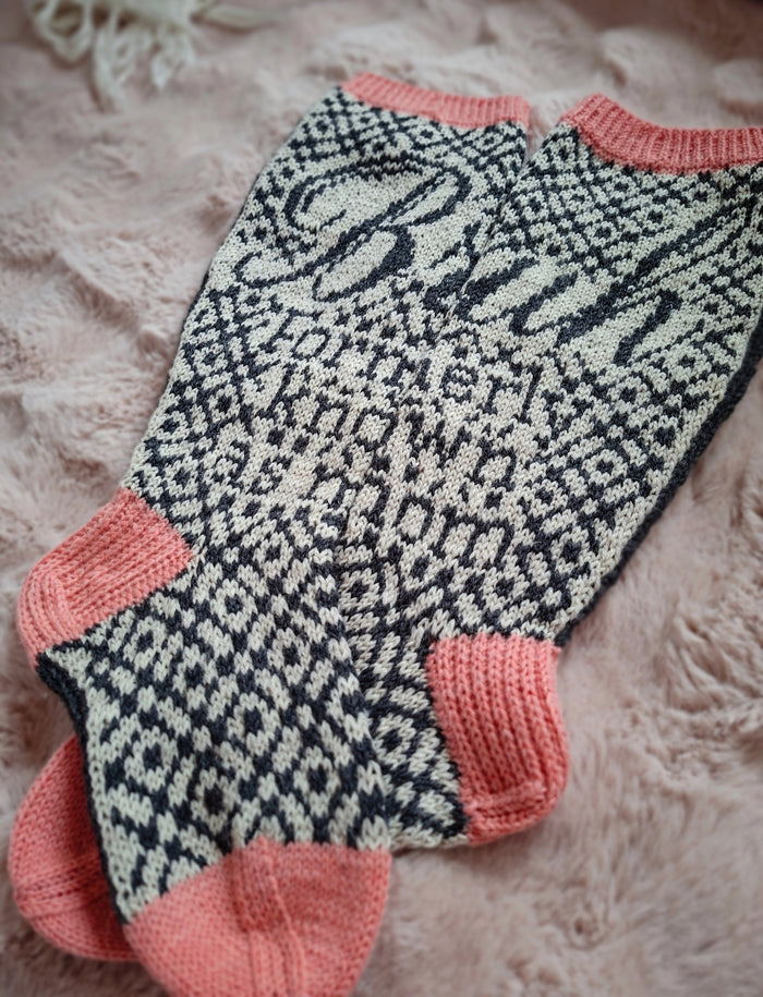Pair of socks with a black and white pattern and pink accents on a soft background