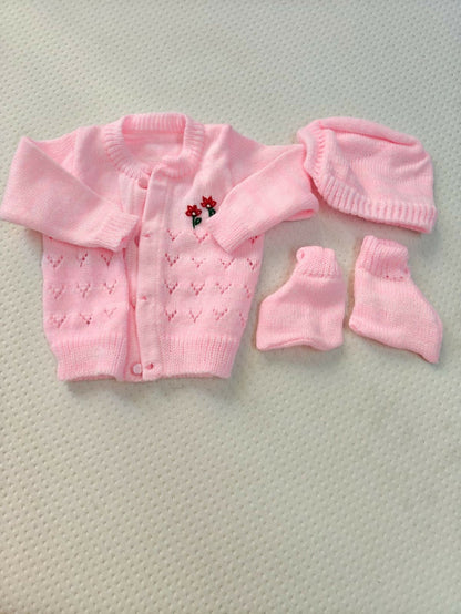 Pink baby cardigan, hat, and booties set on a textured surface