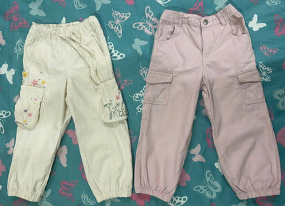 Two pairs of pants, one light green and one pink, on a blue fabric background with butterfly patterns.