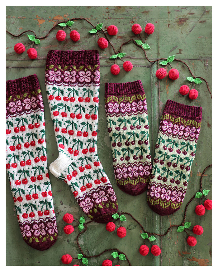 Knitted socks with cherry pattern on a rustic wooden background, surrounded by a crocheted vine with cherries