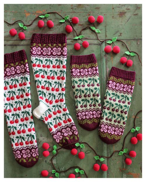 Knitted socks with cherry pattern on a rustic wooden background, surrounded by a crocheted vine with cherries