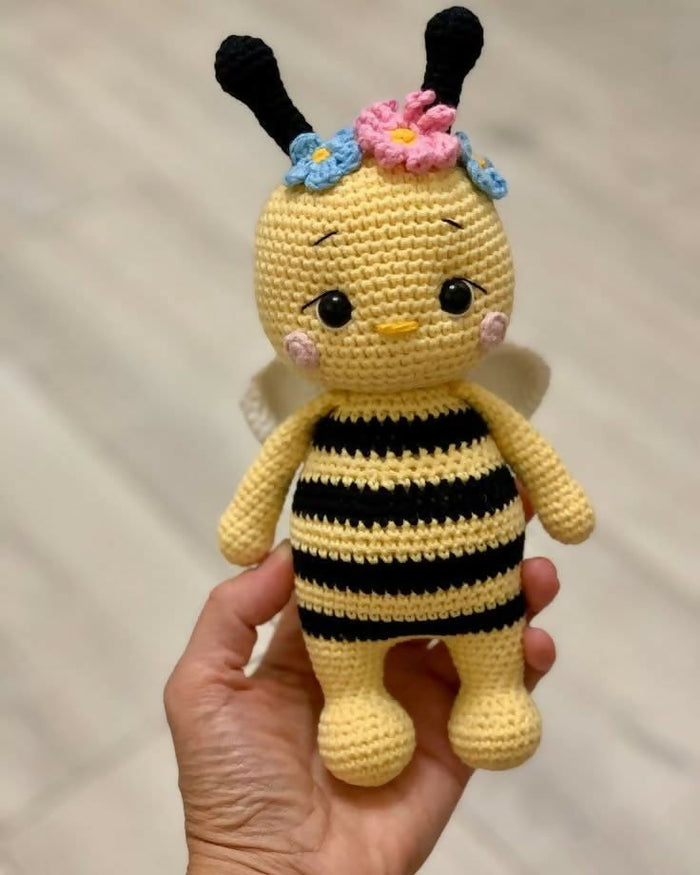 Handmade crochet bee toy held in a hand against a plain background