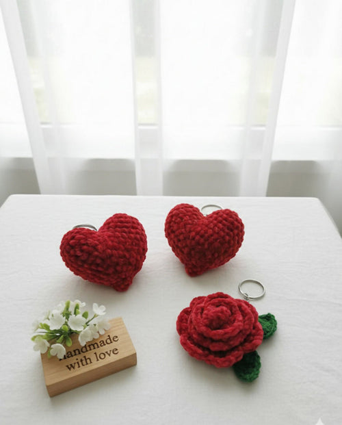 Red heart-shaped and rose-shaped crochet items on a white surface with a 'Handmade with Love' sign.