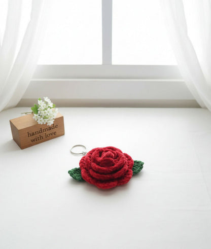 Red rose-shaped keychain on a white surface with a 'handmade with love' sign in the background.