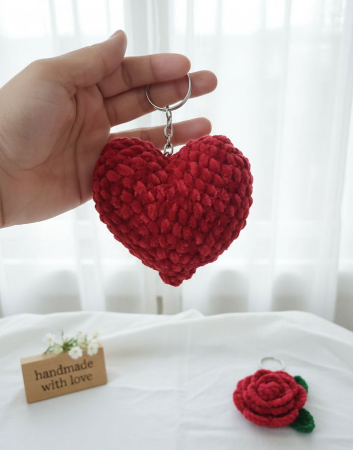 Hand holding a red crocheted heart keychain with a white background