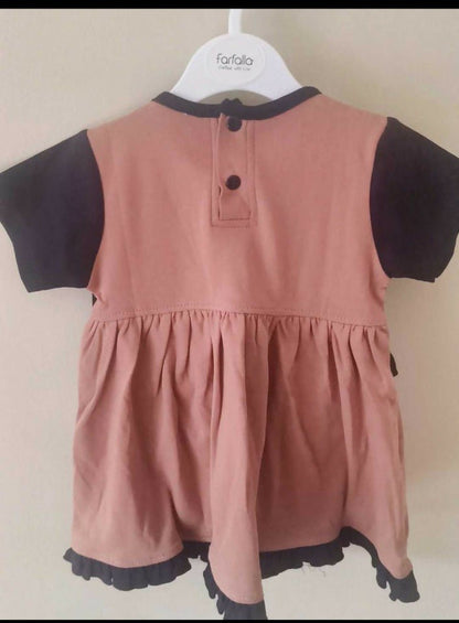 Pink dress with black sleeves and trim on a hanger against a beige background