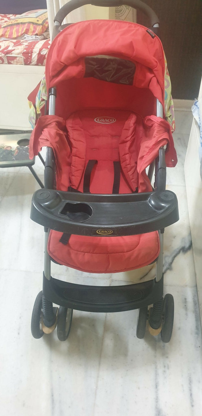 Red stroller with a black tray on a marble floor.