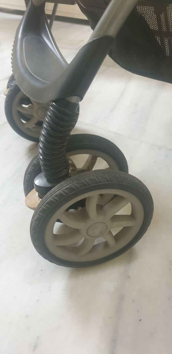 Close-up of a stroller wheel with a spring mechanism on a light-colored floor.