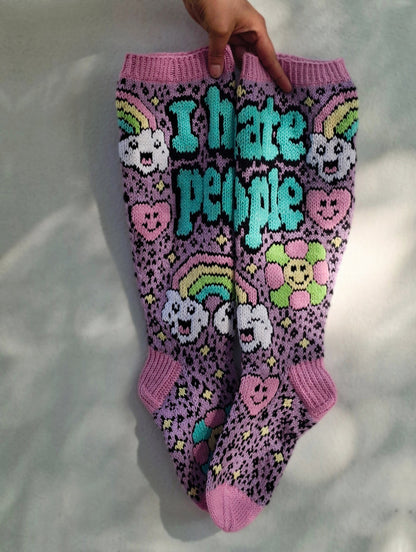 Purple socks with colorful designs and text held by a hand on a white background