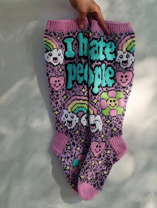 Purple socks with colorful designs and text held by a hand on a white background