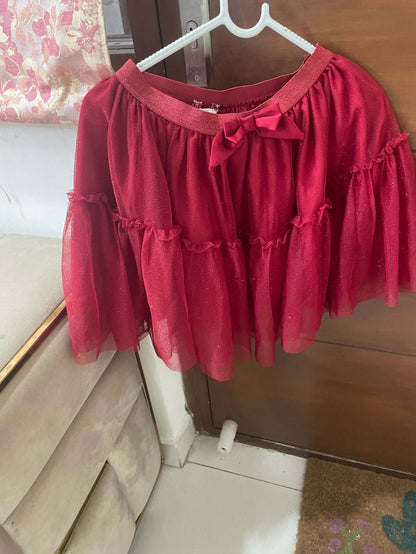 Red blouse with ruffled sleeves and a bow on a hanger against a wooden door.