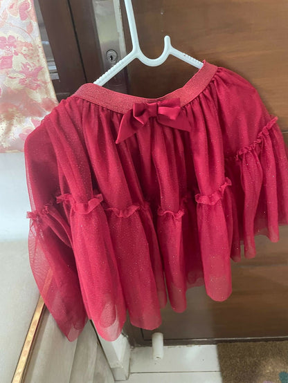Red dress with ruffled sleeves and bottom hanging on a hanger against a wooden door.