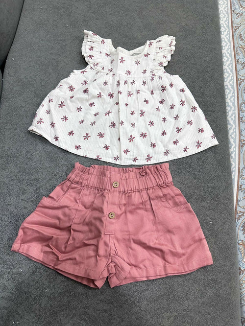 White floral top and pink shorts set on a gray surface