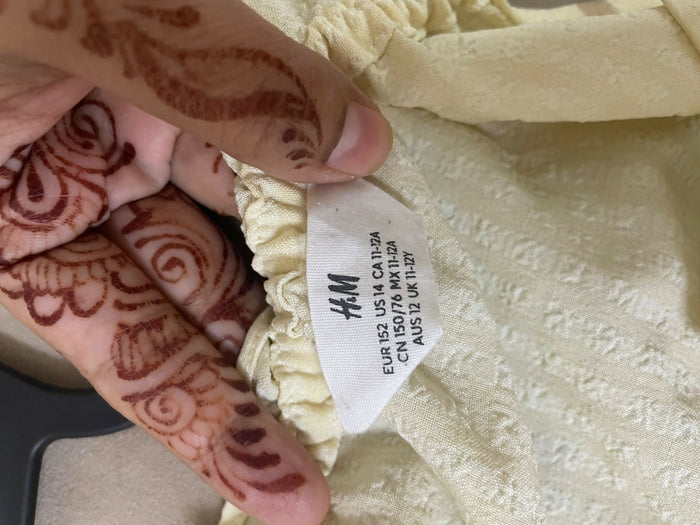 Henna-decorated hand holding a cream-colored garment with an H&M tag.
