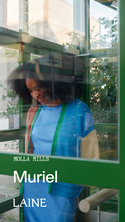 A woman in a blue dress standing in front of a glass structure wearing 'Muriel' designed by Molla Mills