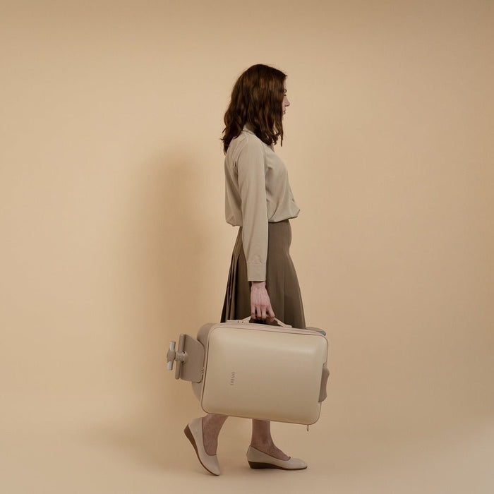 Woman holding a beige suitcase against a beige background