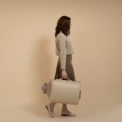 Woman holding a beige suitcase against a beige background
