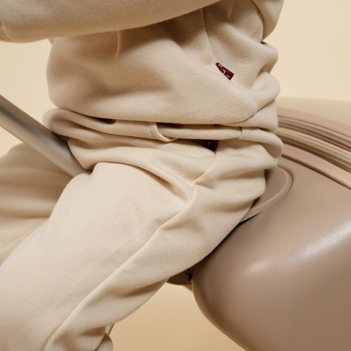 Close-up of beige pants with a small red logo on a beige background