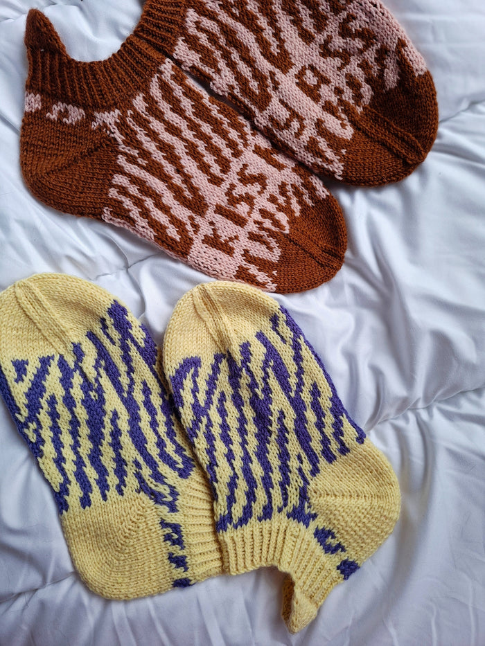 Pair of brown and pink patterned socks and a pair of yellow and blue patterned socks on a white surface.