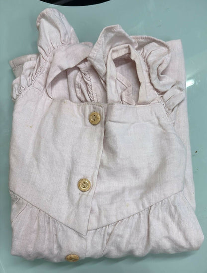 Folded light pink baby outfit with ruffled details on a light blue surface