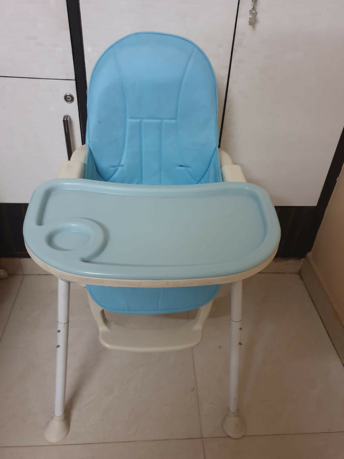 Blue baby high chair with white legs on a tiled floor.