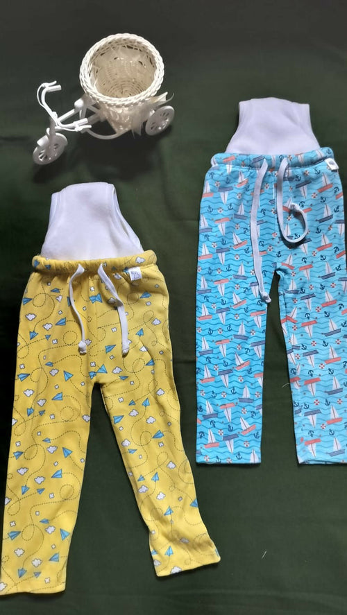 Two pairs of pajama pants, one yellow and one blue with airplane pattern, on a dark surface.