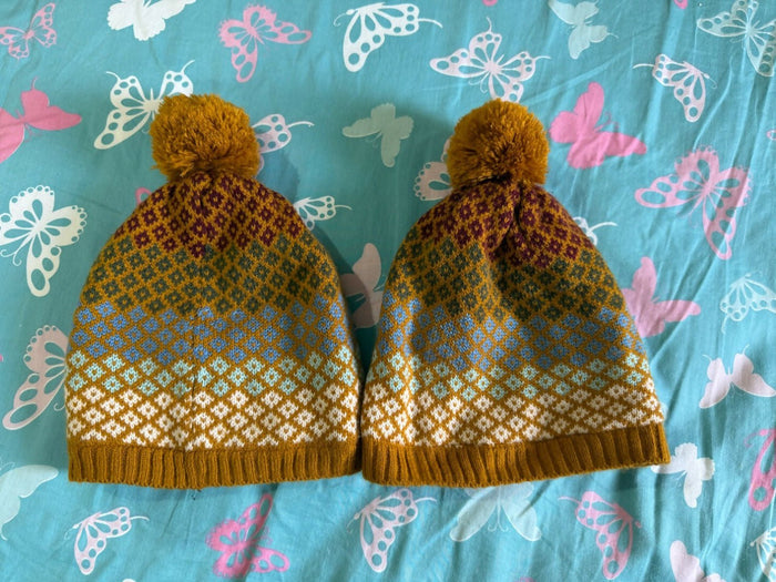Pair of knitted hats with a pattern on a blue fabric background with butterfly designs.