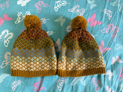 Pair of knitted hats with a pattern on a blue fabric background with butterfly designs.