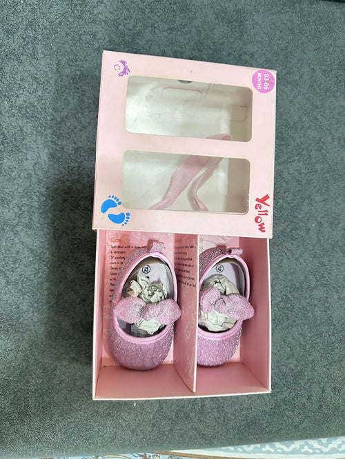 Pink baby shoes with floral design in a box on a gray background